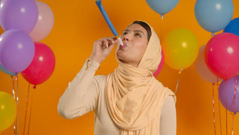 Studioporträt-Einer-Frau-Mit-Hijab,-Die-Geburtstag-Mit-Luftballons-Und-Partygebläse-Feiert